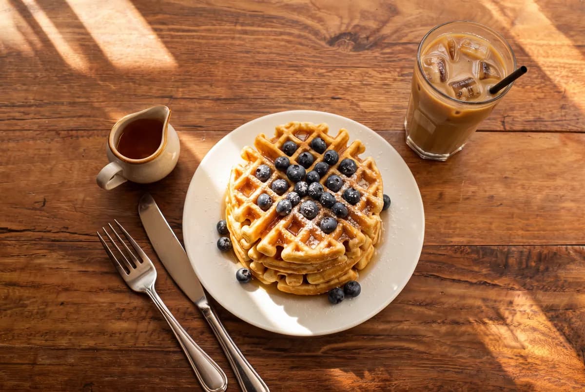 The edit: the same plate now holds blueberry waffles dusted with icing sugar, and the orange juice is an iced coffee.