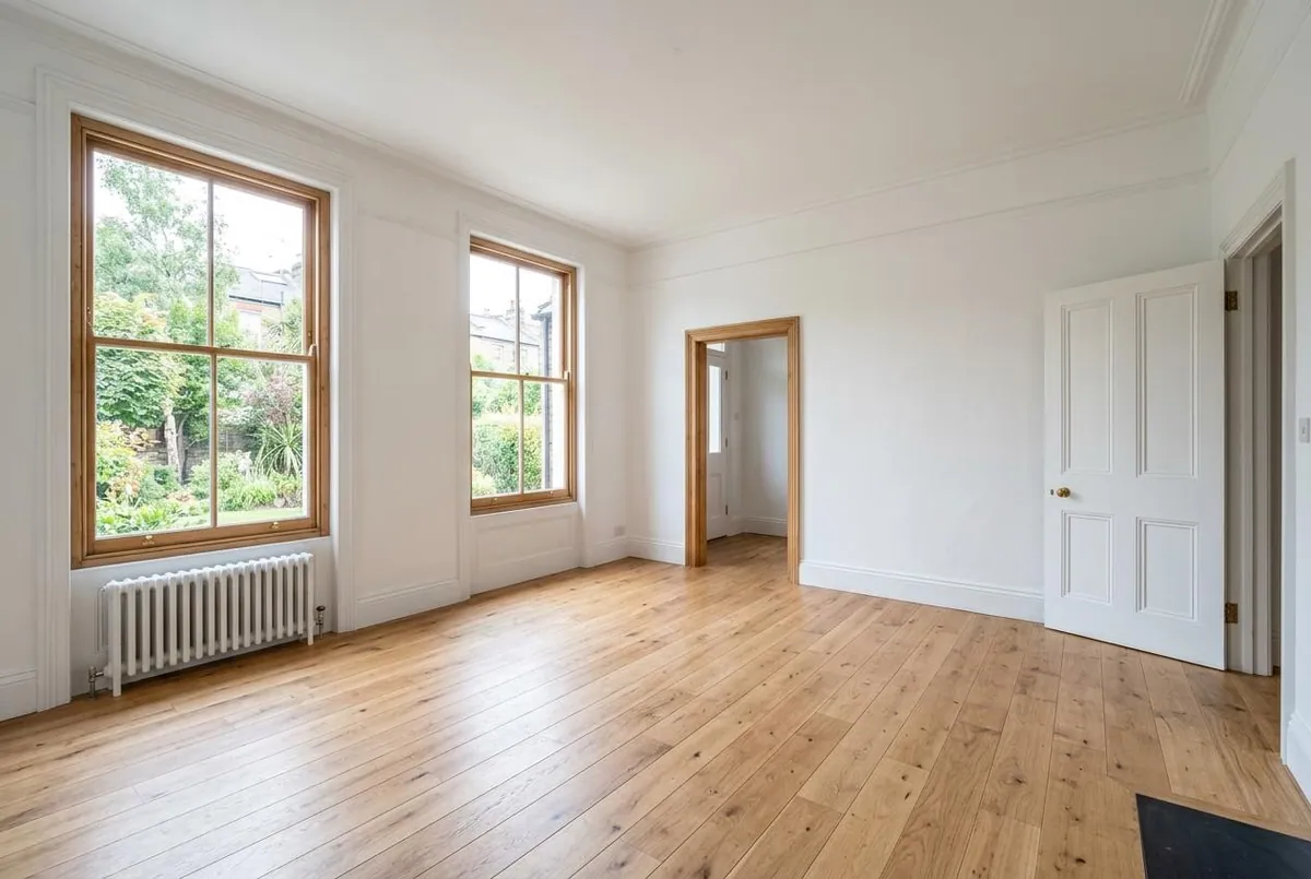 Input: an empty living room with tall sash windows, oak floorboards, a radiator and white walls.